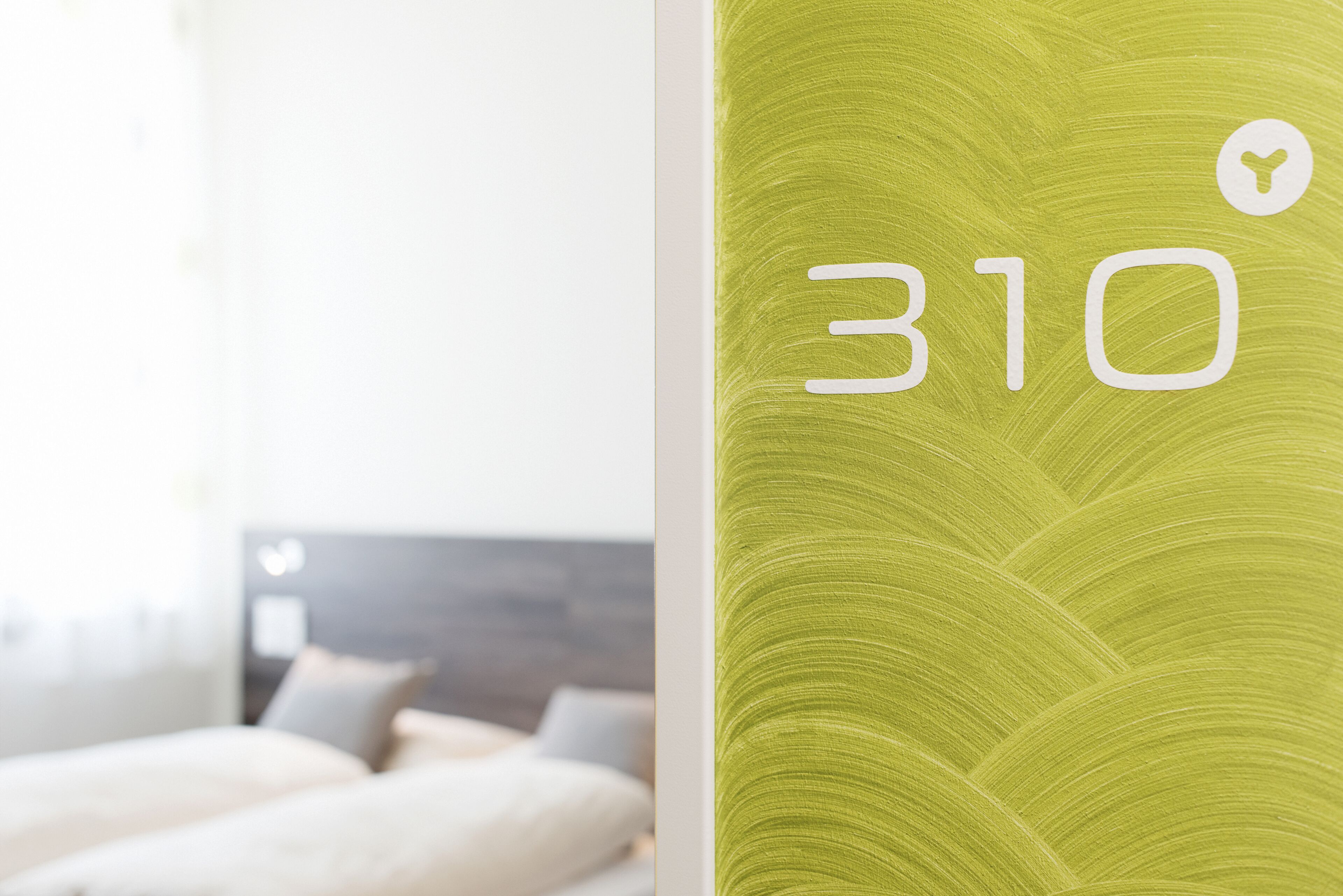 A room with a bed, a headboard, and a wall with a green textured pattern and the number 310.