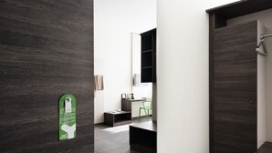Een moderne hotelkamer met donkere houten vloeren, een groene stoel, een kleine tafel en een minibar.
