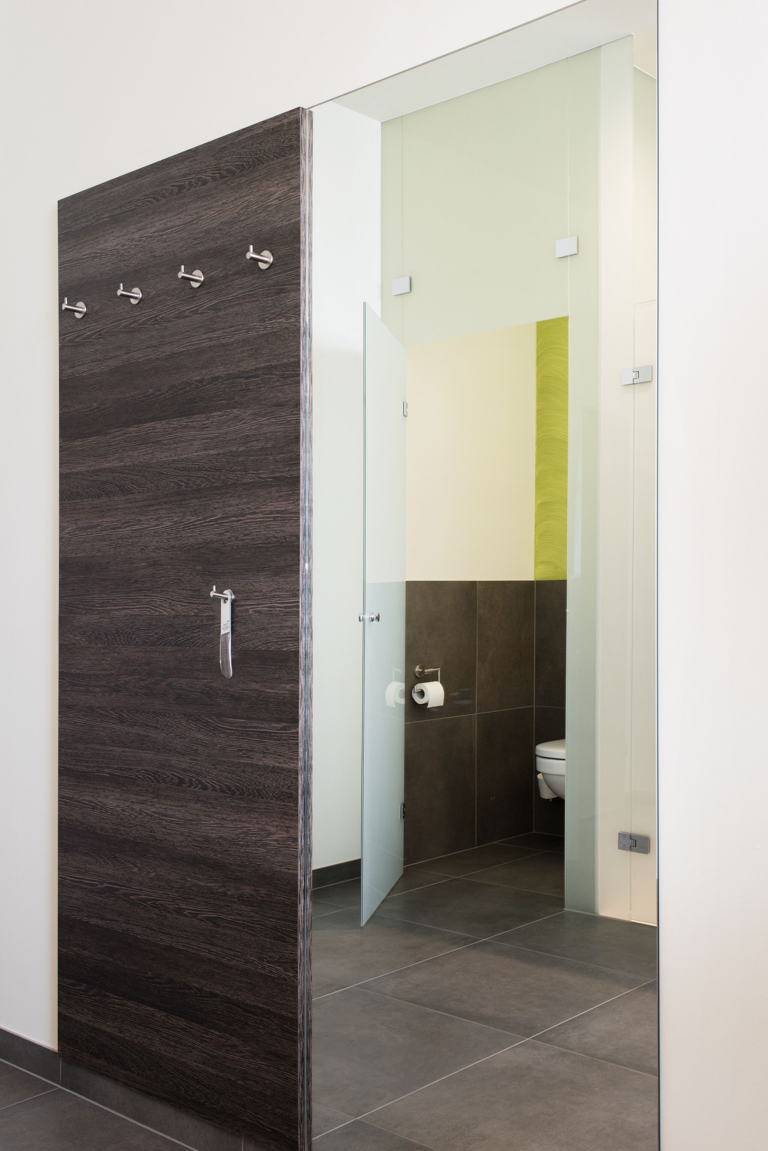 Een moderne badkamer met een donker houten paneeldeur, een glazen douchecabine en een toilet met een wit reservoir.