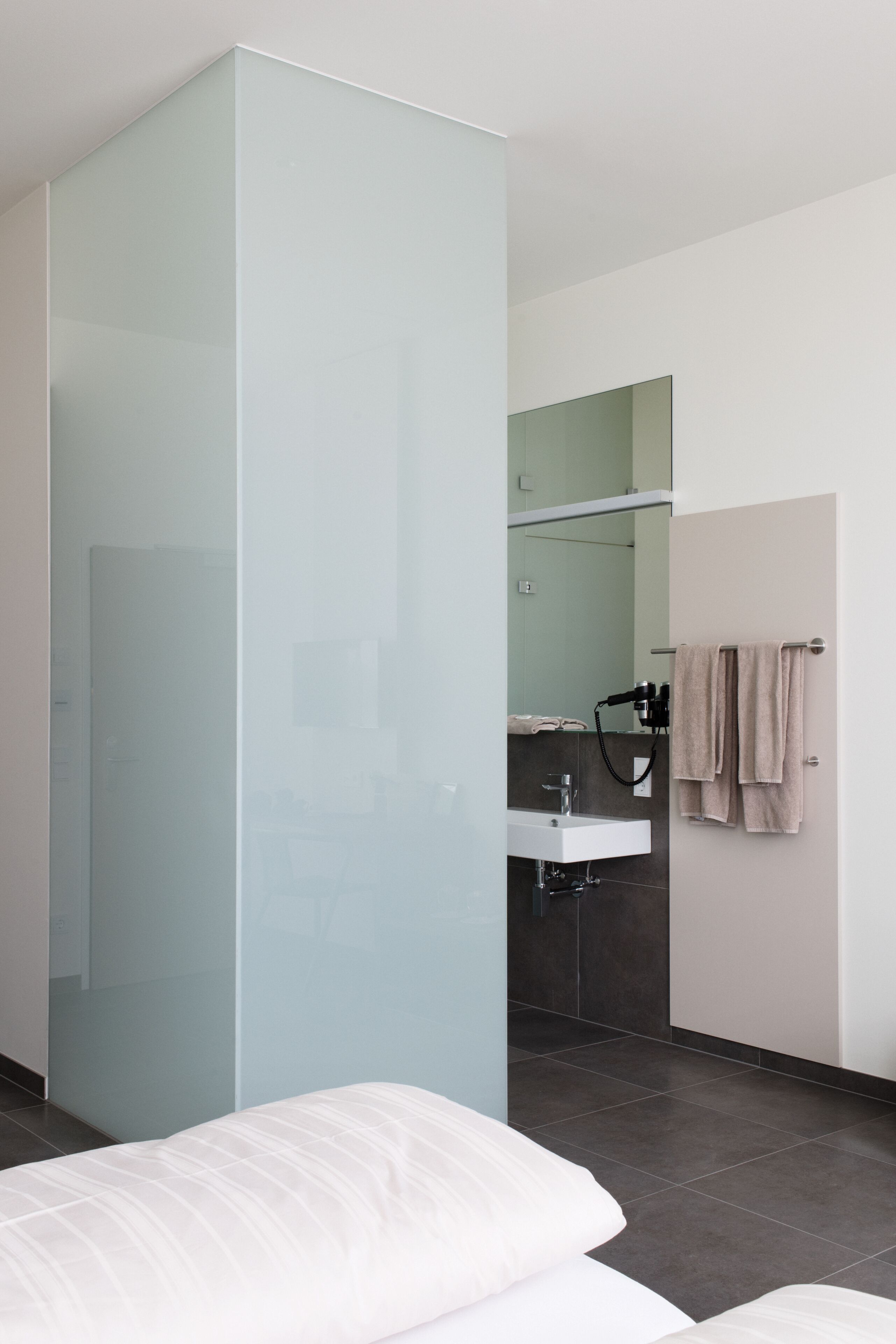 Un baño moderno con mampara de vidrio, lavabo y perchero para toallas.