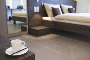 A modern bedroom with a bed, a cup on a saucer, and a mirror reflecting the room. - eee hotel TRAUN (Traun)