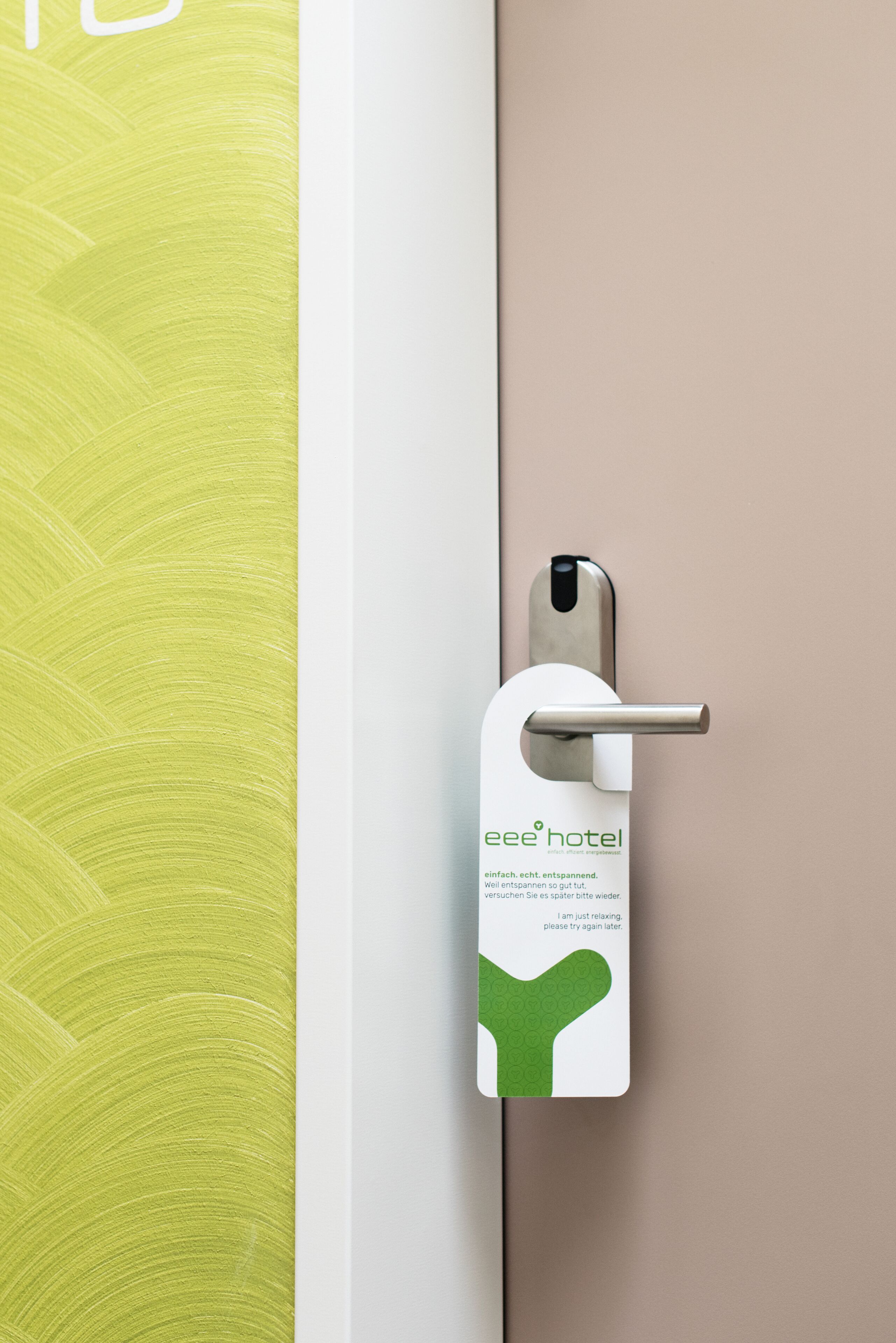 A hotel door with a metallic handle and a green and white tag hanging on it.