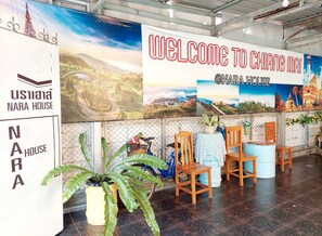 Un área de recepción con un cartel que dice 'Welcome to Chiang Mai', el logo de NARA HOUSE y una bicicleta con una cesta de flores.