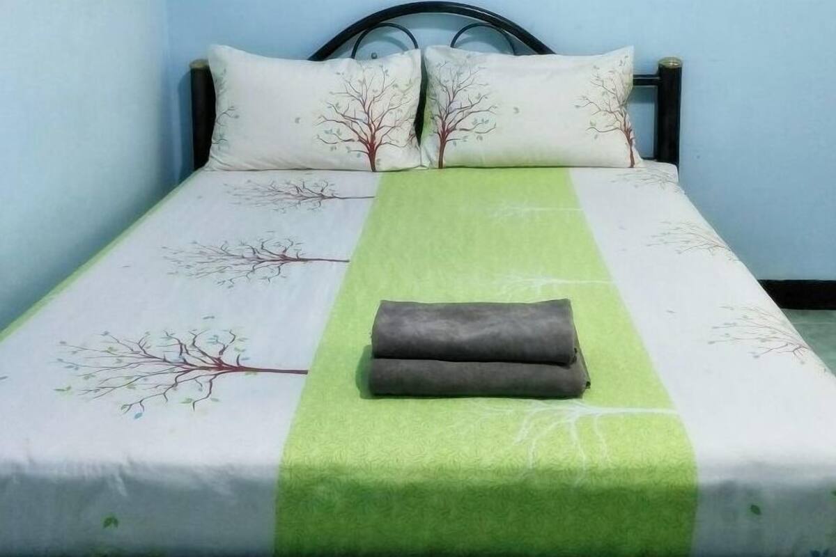 A bed with a green and white bedspread, two pillows with tree designs, and a folded blanket on the bed.