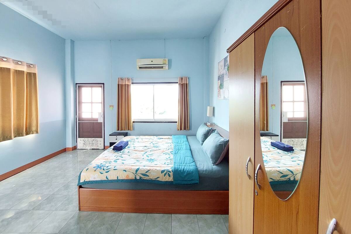 A bedroom with a bed, a wardrobe, a window, and an air conditioning unit.