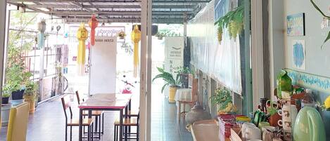 Un área de comedor al aire libre cubierta, con una mesa y sillas, plantas en macetas y faroles colgantes.