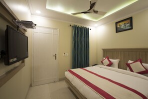 A hotel room with a bed, a television mounted on the wall, a ceiling fan, and a door.