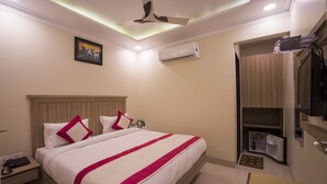 A hotel room with a large bed, a ceiling fan, an air conditioning unit, a small desk with a phone, and a wardrobe.