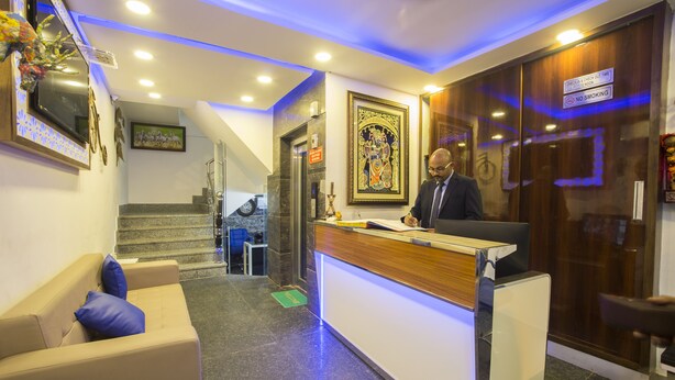 A hotel reception area with a reception desk, a sofa with blue cushions, a staircase, and a framed artwork on the wall.
