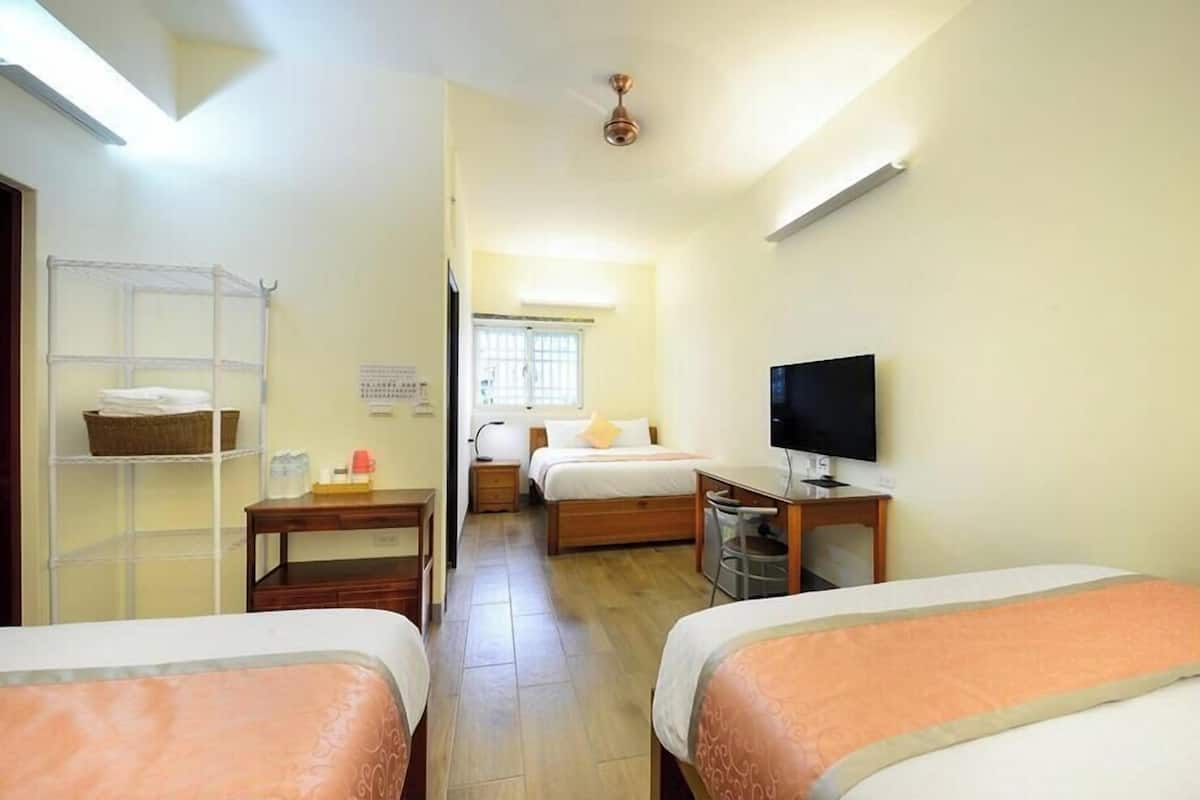 A hotel room with two beds, a TV, a desk, a shelf, and a window.