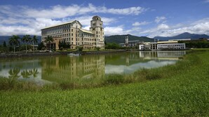 A large building with a prominent tower, a calm lake reflecting the structure, and lush greenery in the foreground. - Yue Mei B&B (Shoufeng)