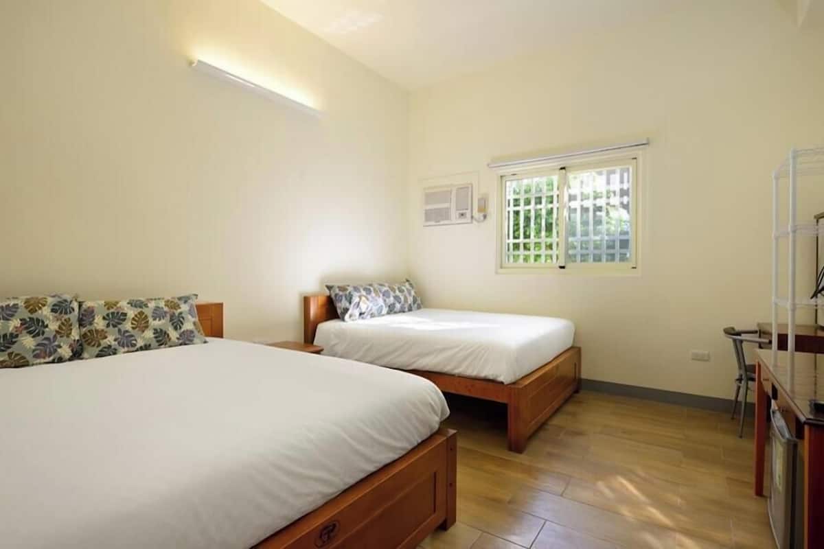 A bedroom with two wooden beds, a small window with a view, and a kitchenette area.