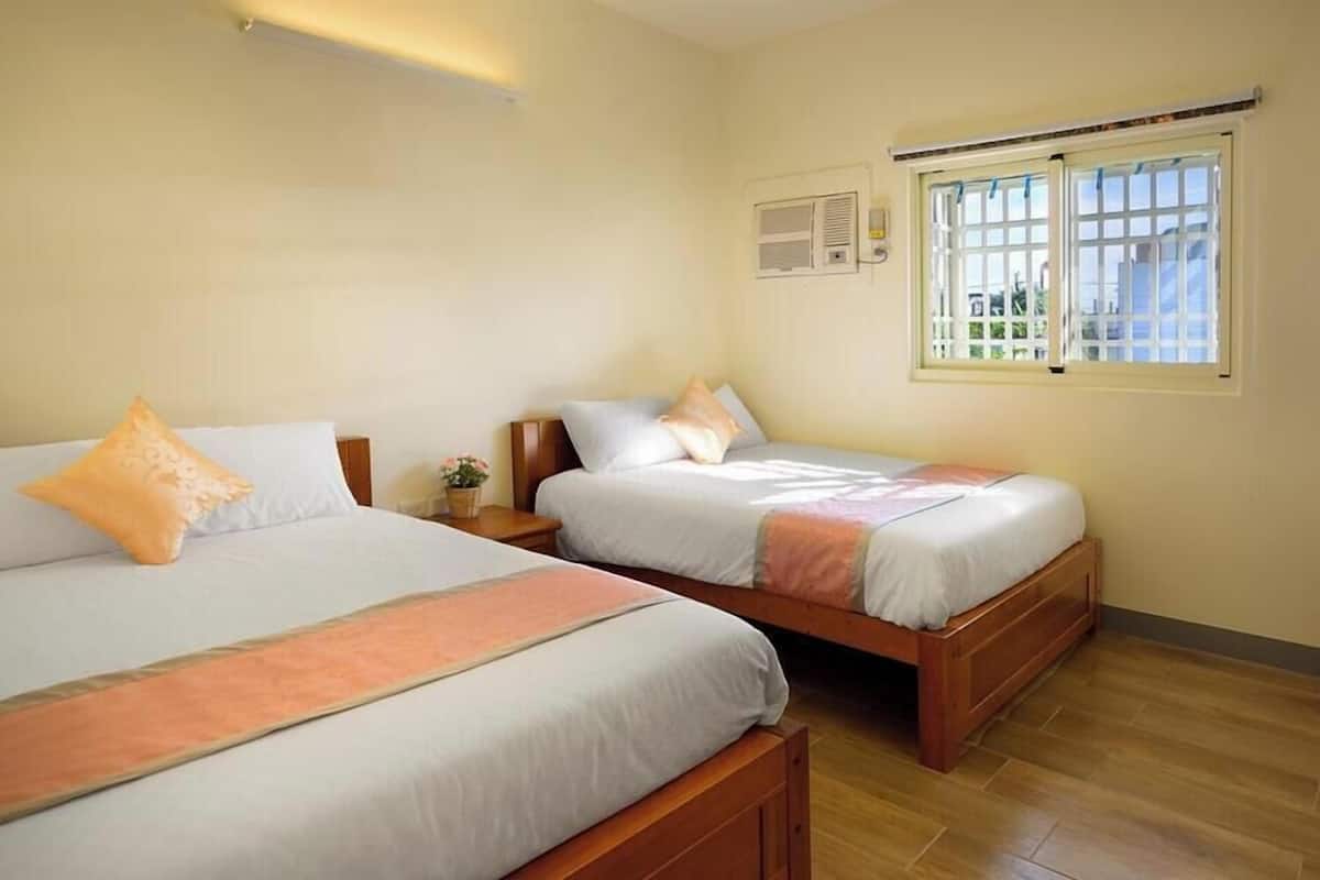 A hotel room with two wooden beds, a window with bars, and a small table with a plant.
