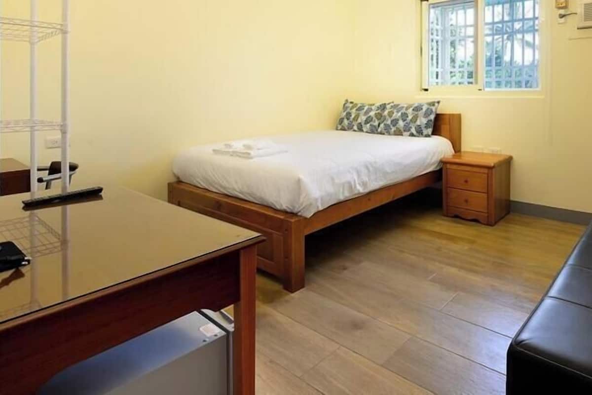 A bedroom with a bed, bedside table, and a black leather sofa.
