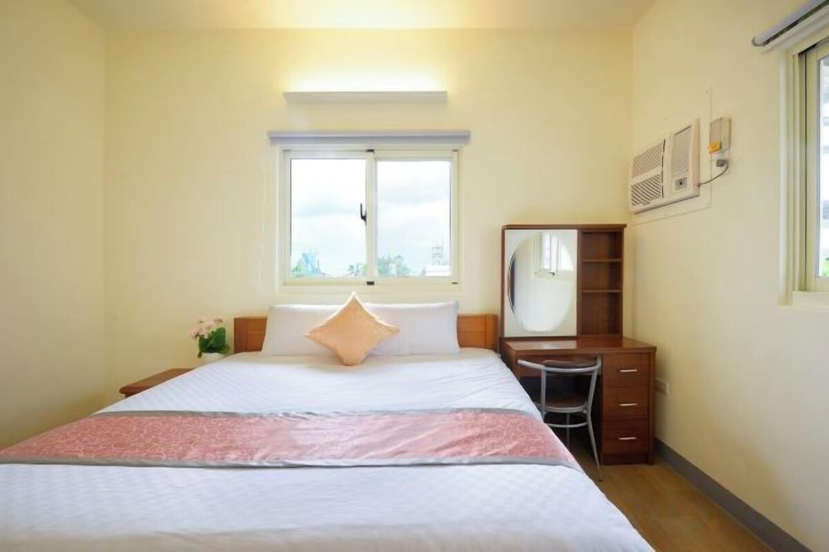 Een hotelkamer met een bed, bureau, stoel, raam en spiegel.