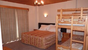 Un dormitorio con una cama doble, una cama individual, un cabecero de madera, una araña y una mesita de noche, además de una ventana con cortinas.
