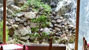 Una habitación con vista a una cascada rocosa, una silla de madera y una mesa con mantel rojo.