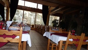 Un restaurante con mesas y sillas de madera, manteles blancos y una pared de piedra al fondo.