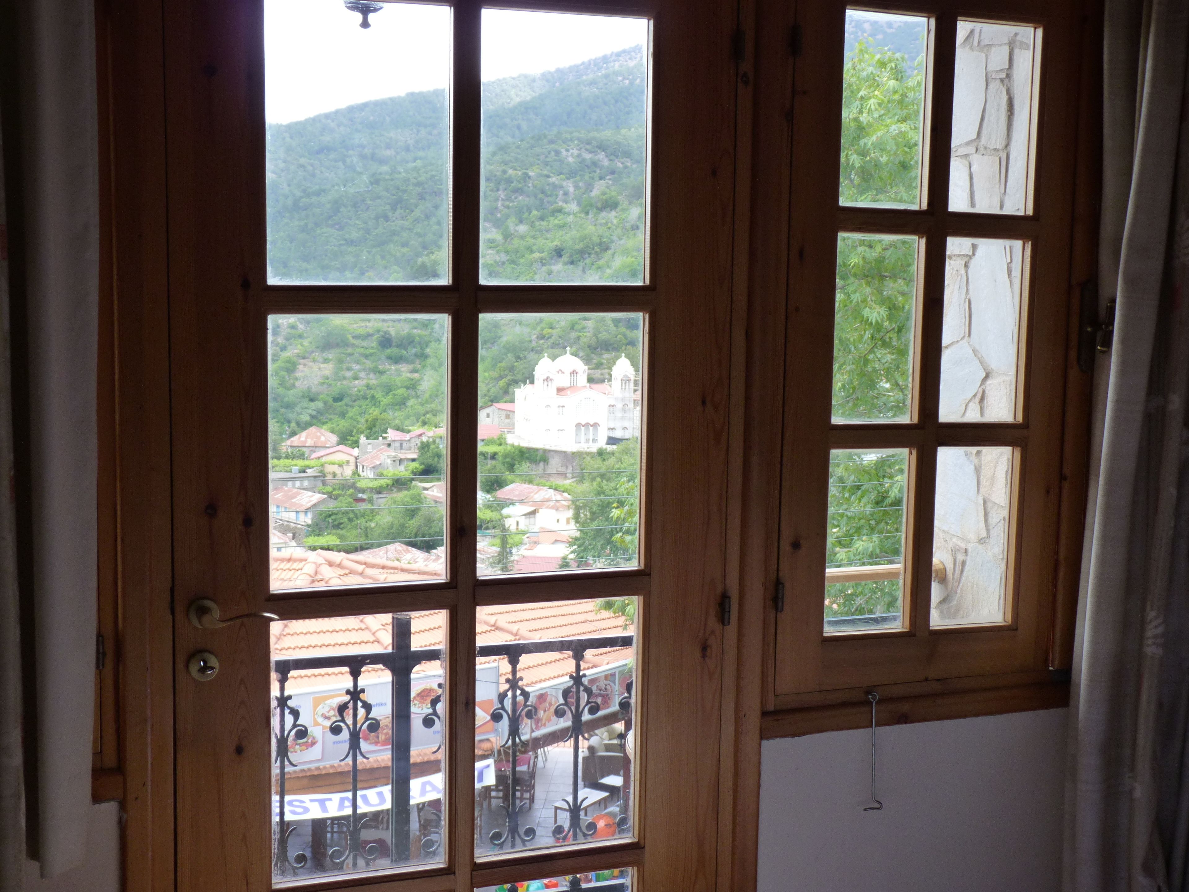 Una puerta de madera con varios paneles de vidrio que muestra una vista de un paisaje montañoso y un edificio blanco con cúpulas.