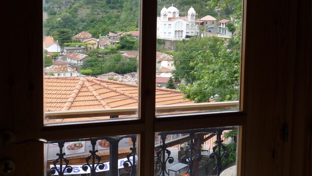 Vista desde una ventana con balcón, mostrando una colina con edificios y vegetación.