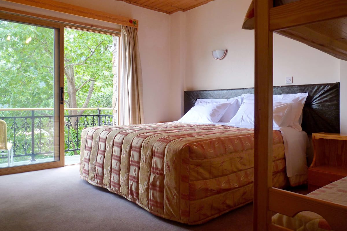 Un dormitorio con cama, cabecera de madera, mesita de noche y ventana con cortinas.