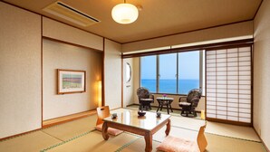 A traditional Japanese room with tatami flooring, a low table, two chairs, and a view of the sea through shoji screens. - Ibusuki Phoenix Hotel (Ibusuki)