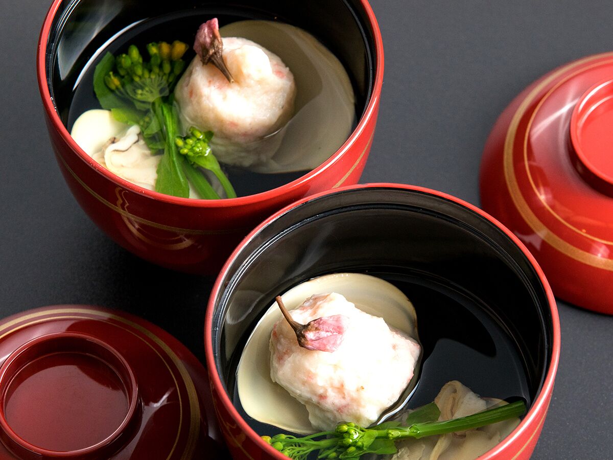 Three red ceramic bowls with a white substance and green garnish, placed on a dark surface.