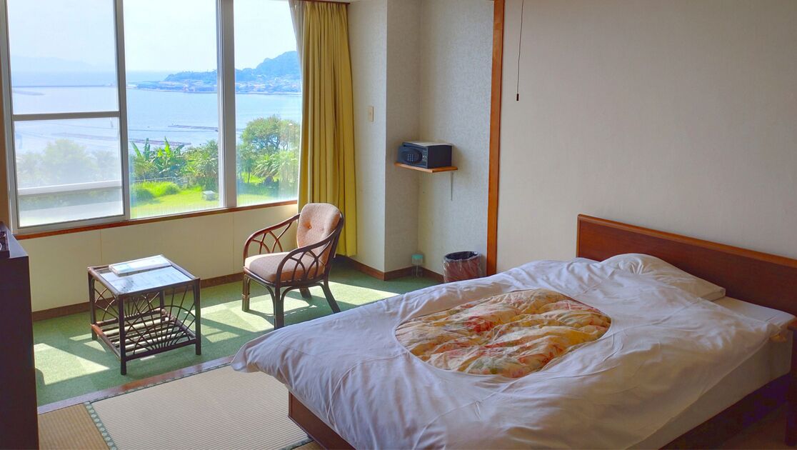 Ein Hotelzimmer mit Bett, Sessel, kleinem Tisch, Ablagefläche und Meerblick.