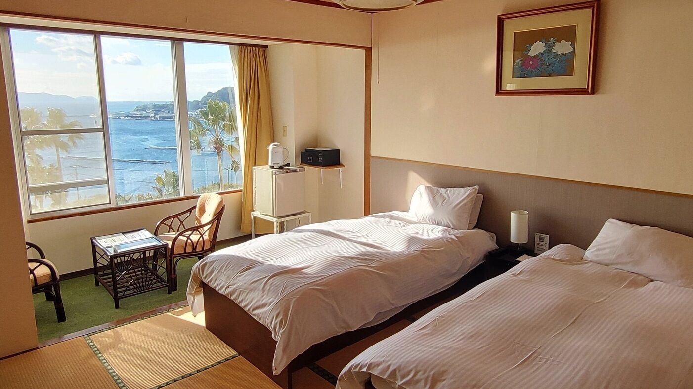 Ein Hotelzimmer mit zwei Betten, Meerblick, einem Sessel, einem kleinen Tisch und einem gerahmten Bild an der Wand.