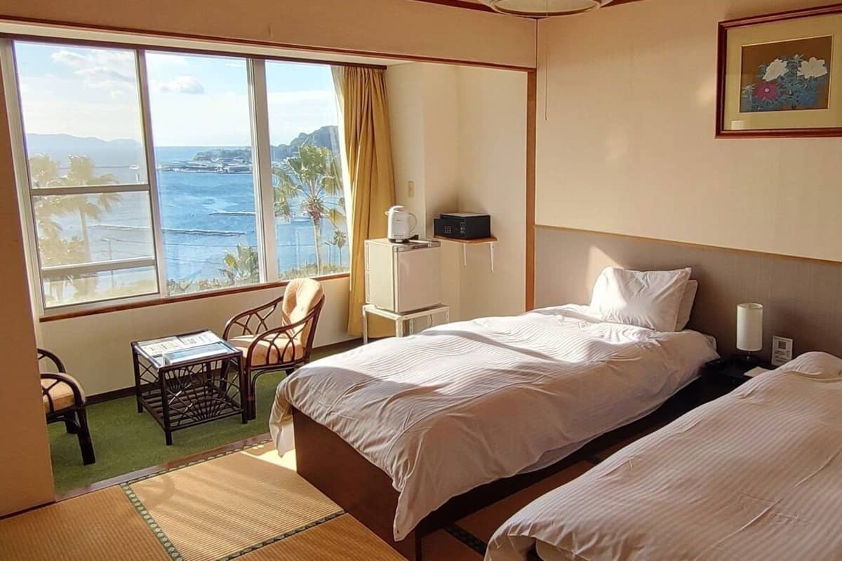 A hotel room with two beds, a view of the ocean, a chair, a small table, and a framed picture on the wall.