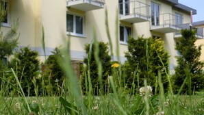 Un immeuble résidentiel à plusieurs étages, doté de balcons, entouré de verdure et surplombant un ciel dégagé.