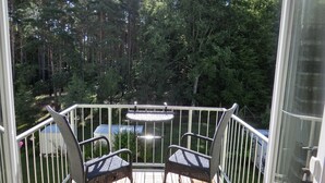 Un balcon avec deux fauteuils en osier et une petite table, donnant sur une zone boisée.
