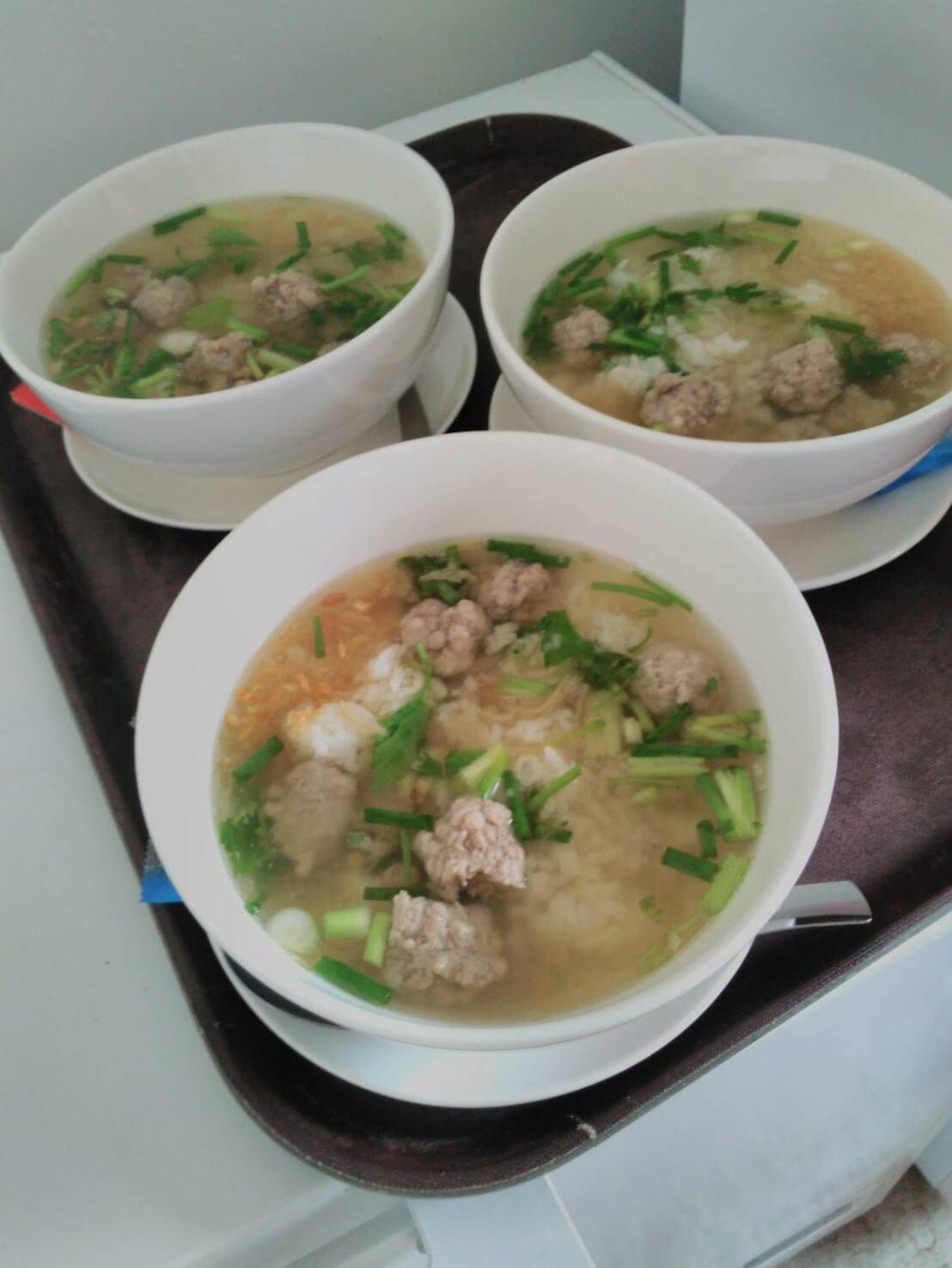 Trois bols de soupe aux boulettes de viande et aux oignons verts, présentés sur un plateau.