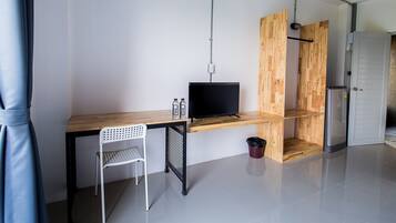 Een moderne, minimalistisch ingerichte kamer met een houten bureau, een televisie, een witte stoel en een kleine prullenbak.