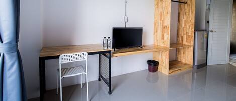 A modern, minimalist room with a wooden desk, a television, a white chair, and a small trash bin.
