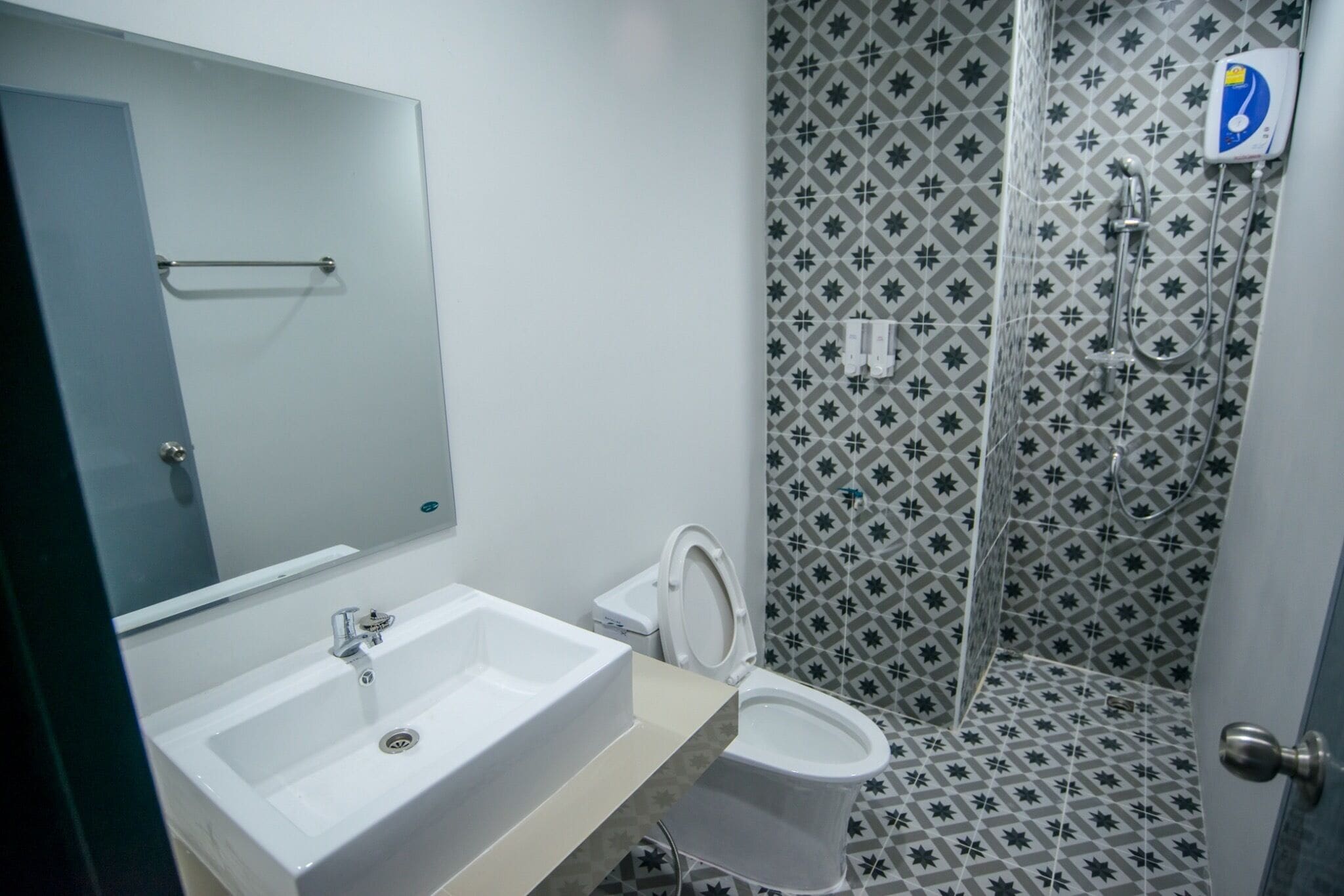 Un baño con lavamanos, inodoro y ducha blancos. Las paredes presentan un diseño geométrico con baldosas.