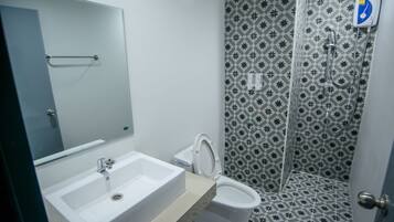 Un baño con lavamanos, inodoro y ducha blancos. Las paredes presentan un diseño geométrico con baldosas.