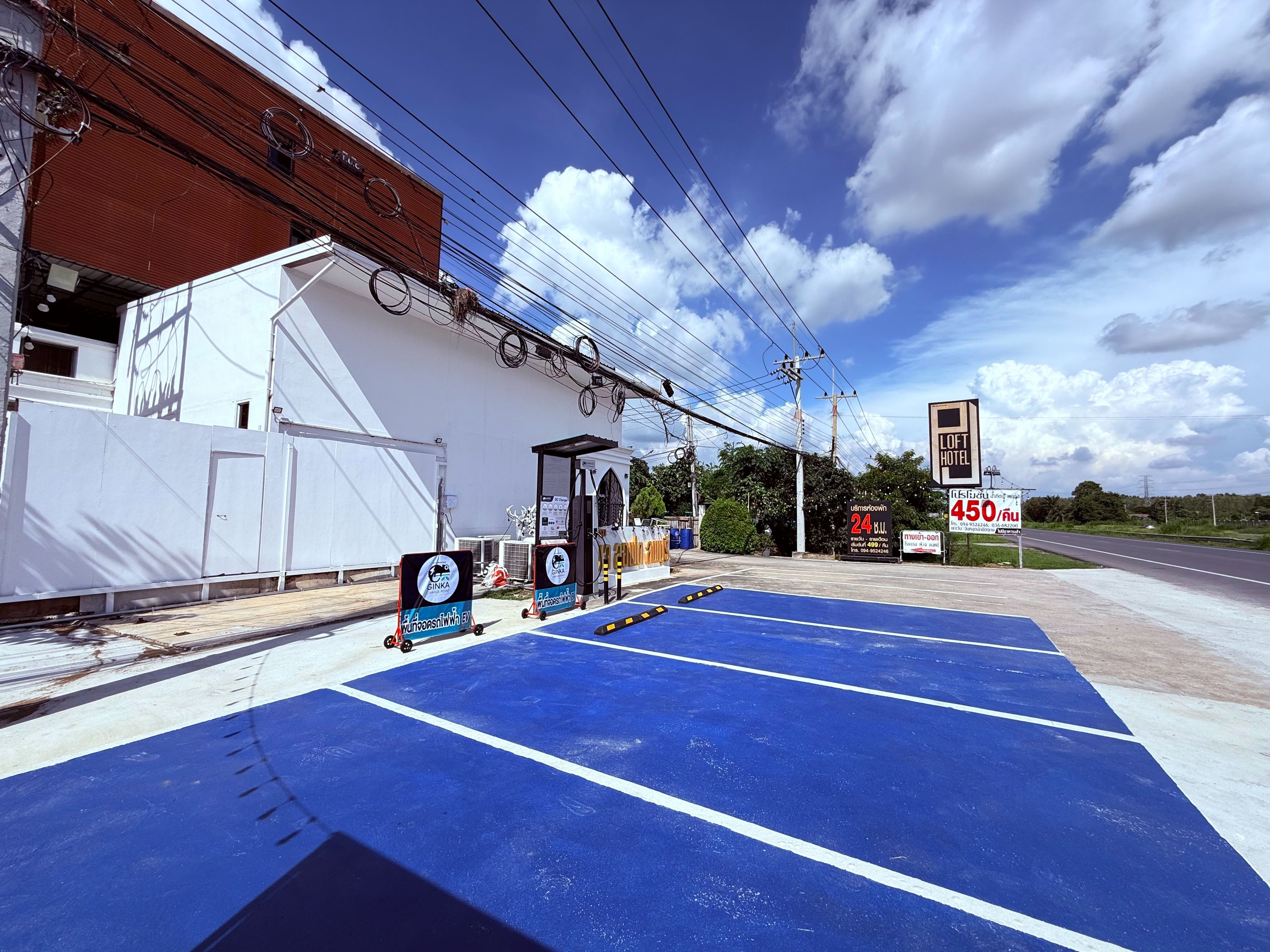 A parking area with blue markings, a building with a white facade, and a sign for a hotel with a price tag.