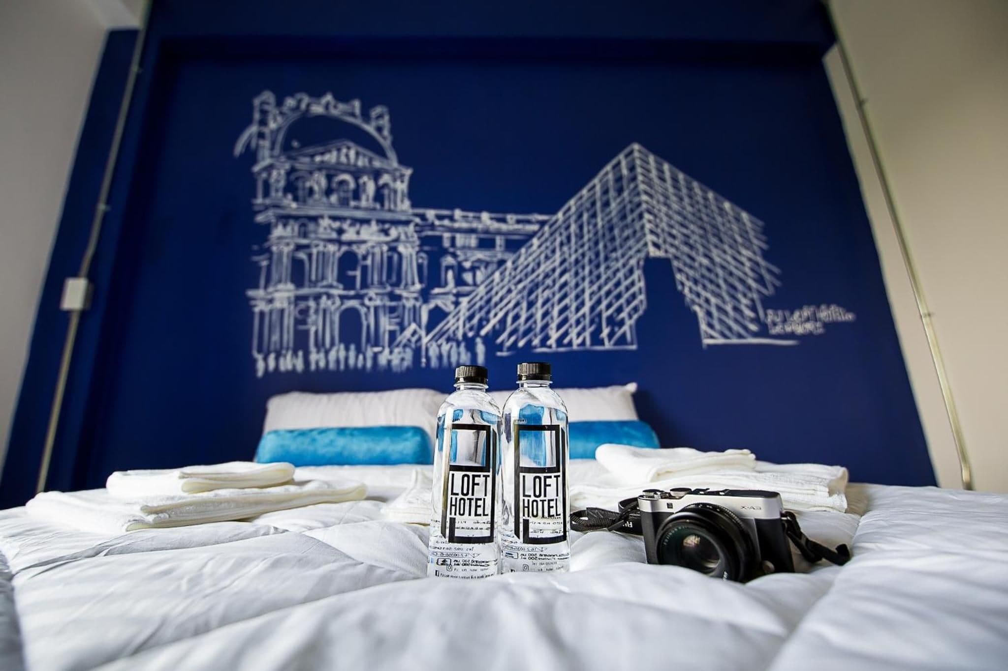 Una cama con dos botellas de agua, una cámara y un almohadón con diseño azul y blanco.