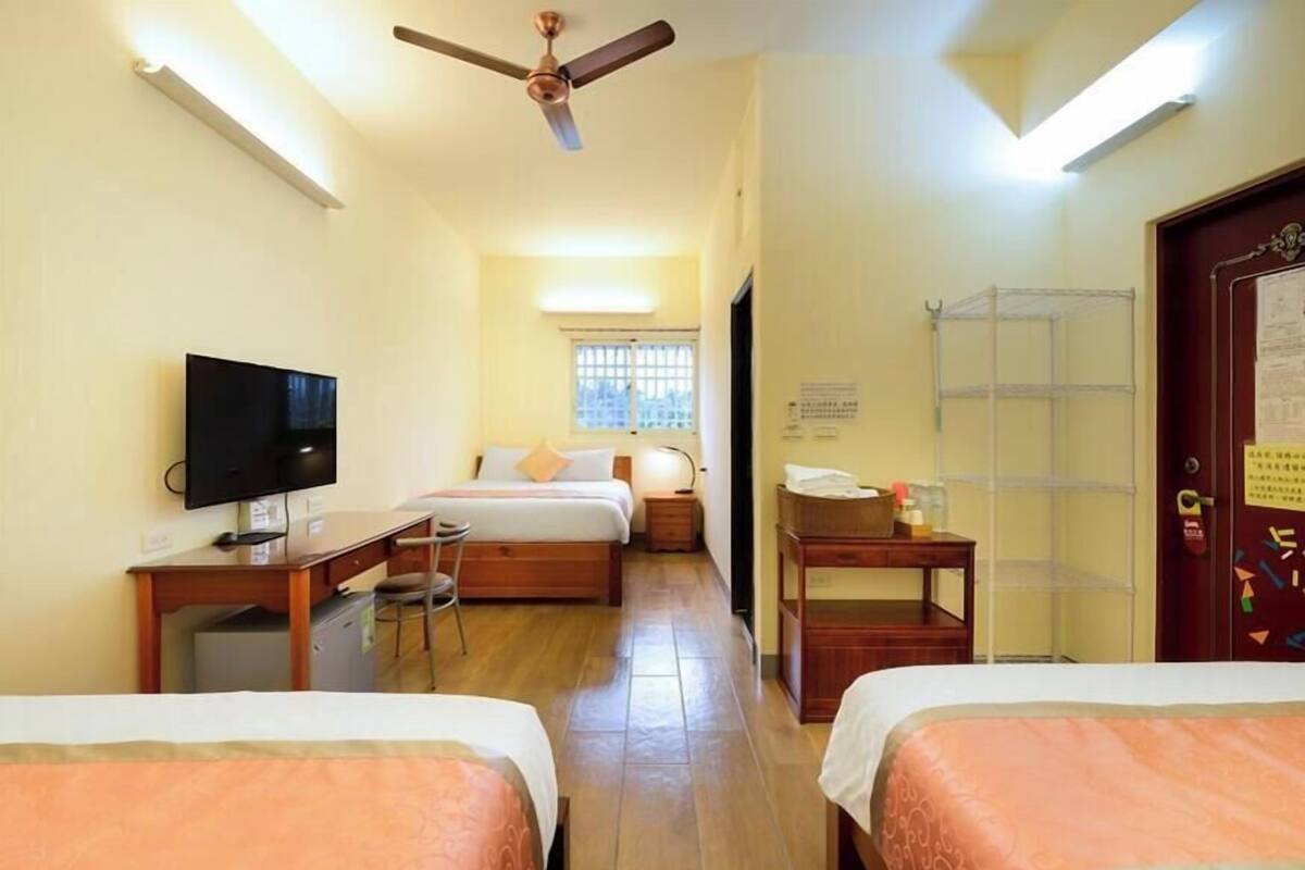 A hotel room with two beds, a desk with a computer, a television, and a ceiling fan.