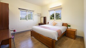 A bedroom with a wooden bed, two bedside tables, a chair, and two windows with views of greenery. - Mei Cun B&B (Shoufeng)
