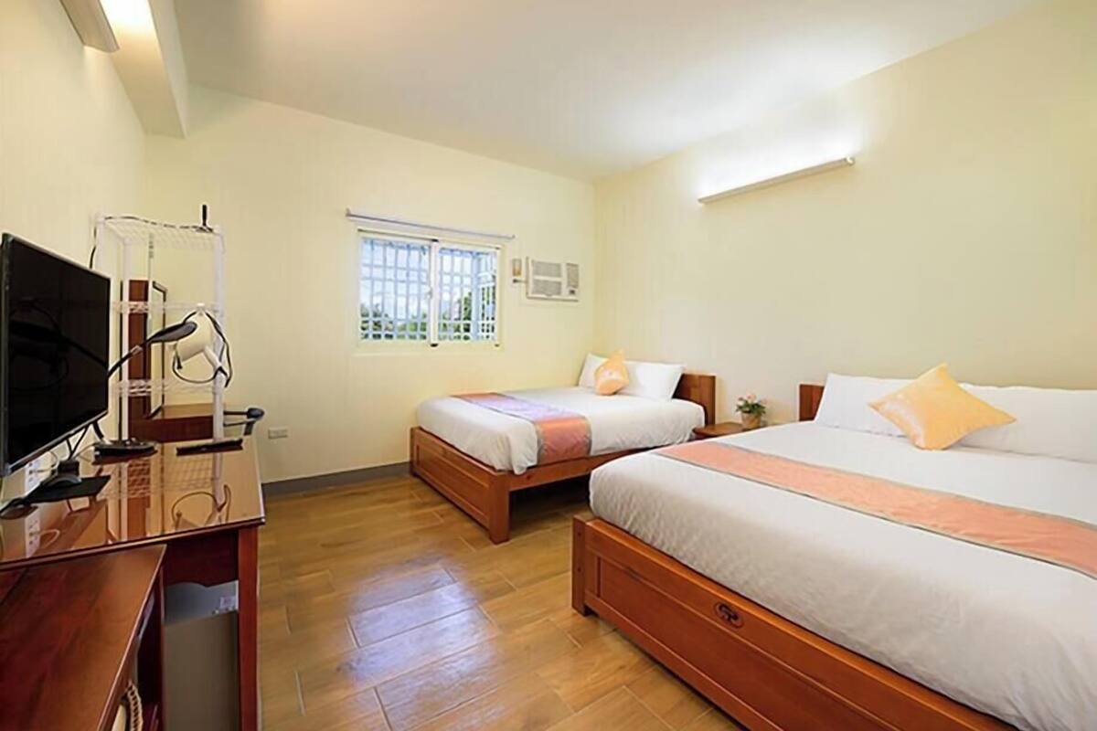 A hotel room with two beds, a desk with a television, and a window with bars.