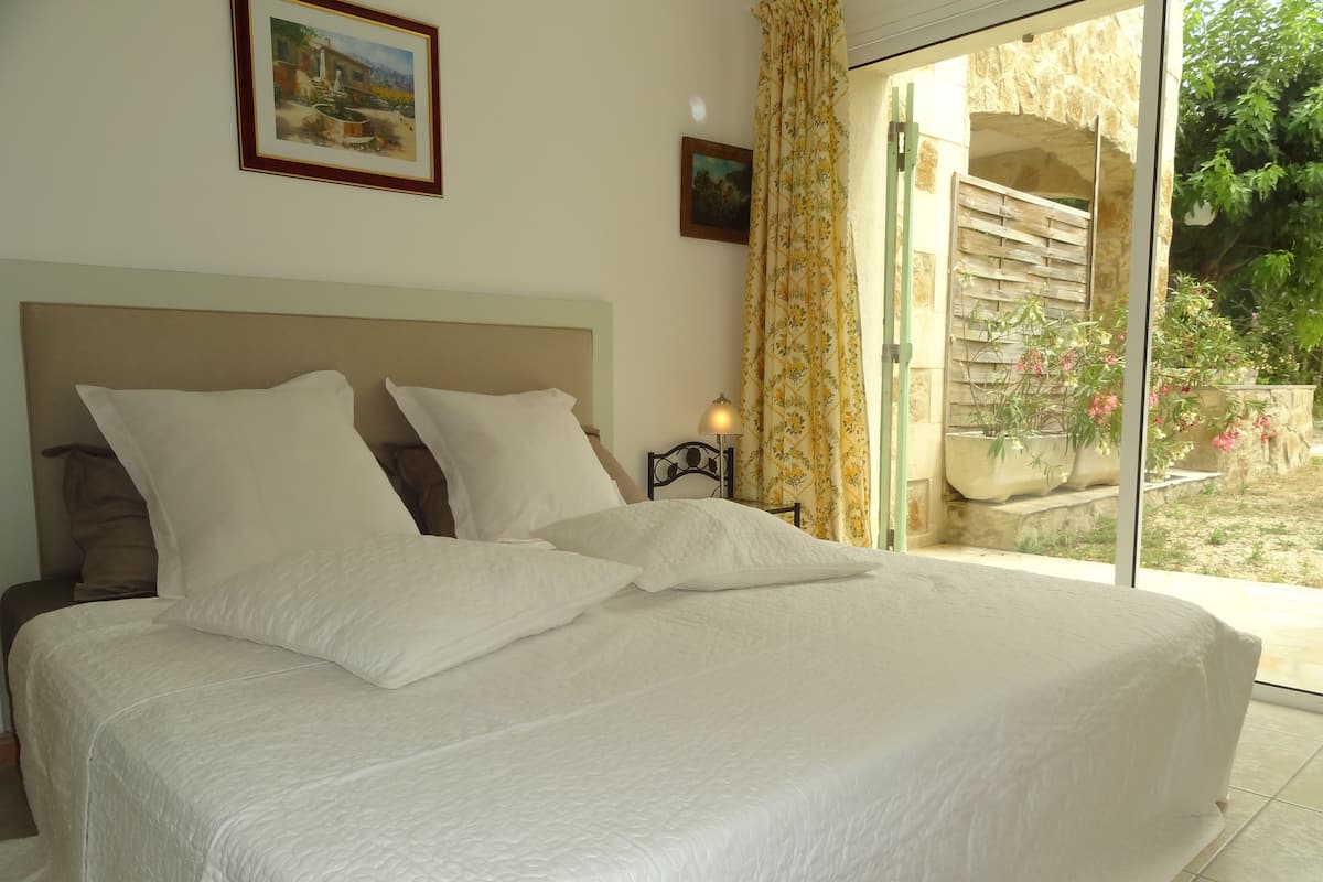 A neatly made bed with white linens in a room with a large window and a view of the outdoors.