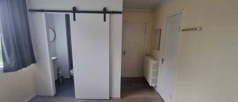 Un dormitorio con una cama, una puerta corredera que da a un baño y un radiador en la pared.