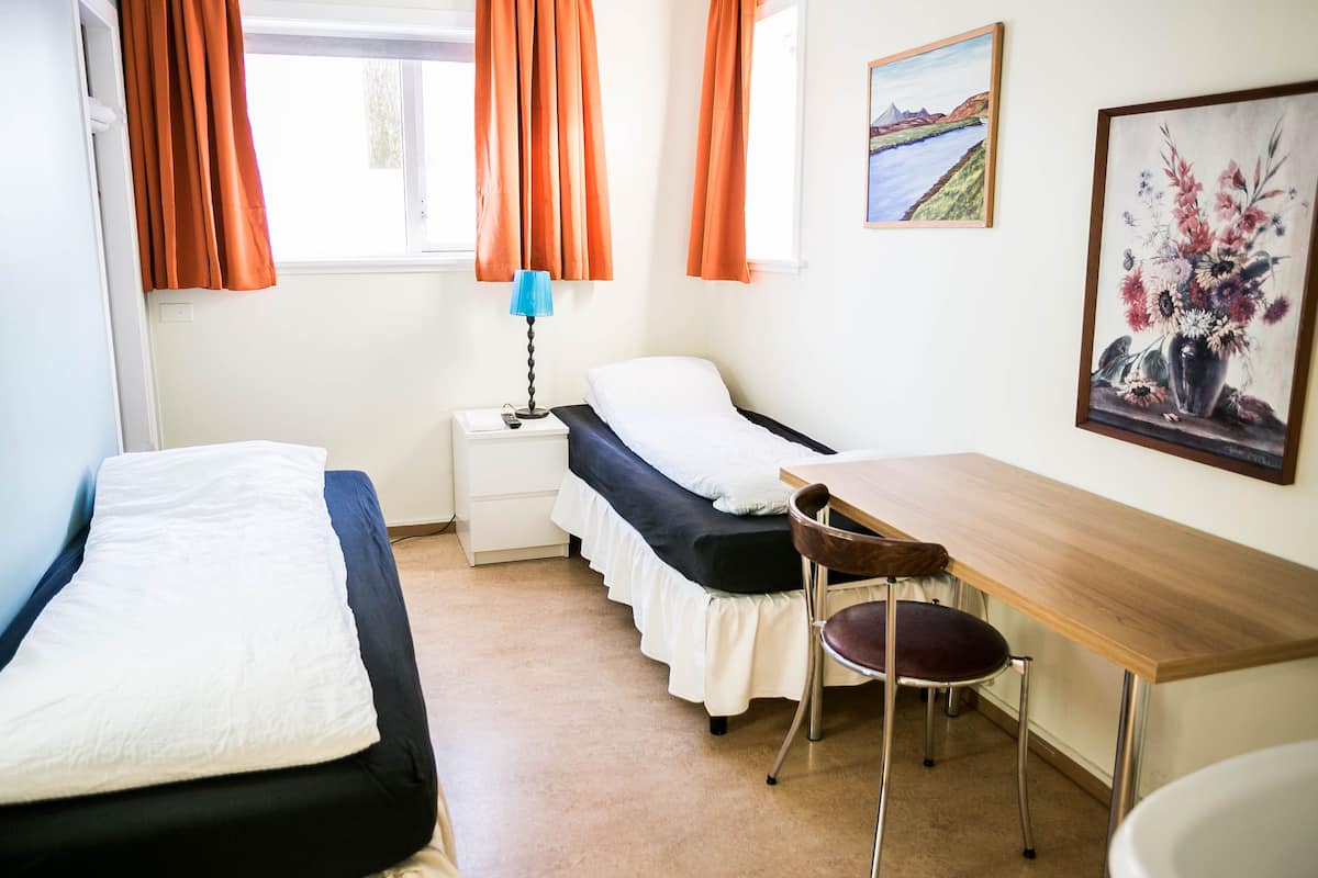 Une chambre avec deux lits, un bureau, une chaise, une lampe et un tableau au mur.
