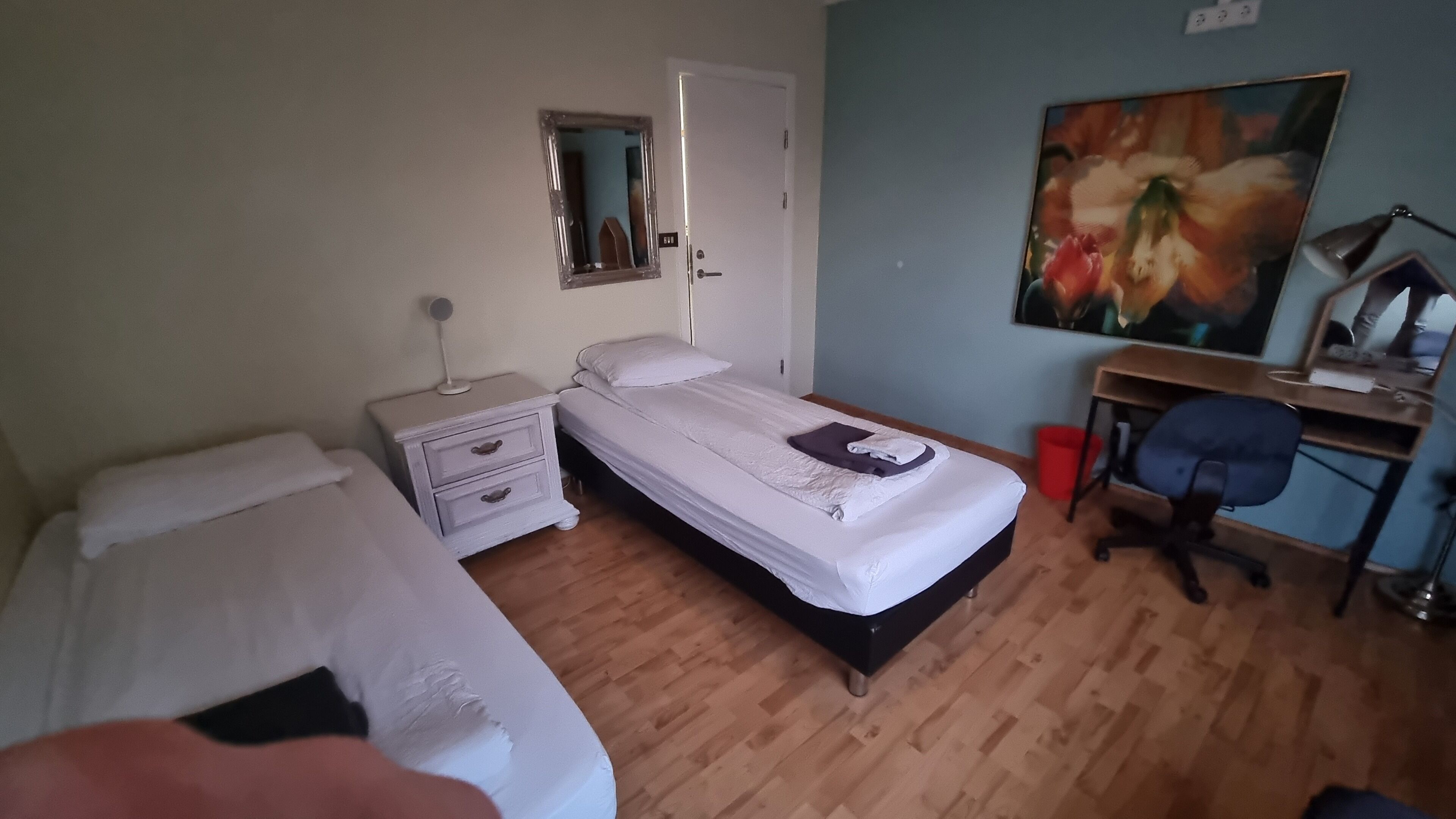 A bedroom with a bed, a desk, a chair, and a painting on the wall.