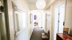 Un couloir orné d’un lustre, avec un banc et une bibliothèque contenant un guide pour les visiteurs.
