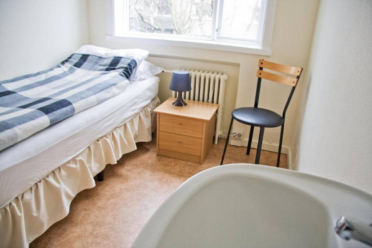 Une chambre à coucher avec un lit, une table de chevet avec une lampe, une chaise et un radiateur.