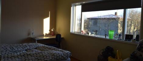 Un dormitorio con cama, escritorio y ventana con vista a una casa.