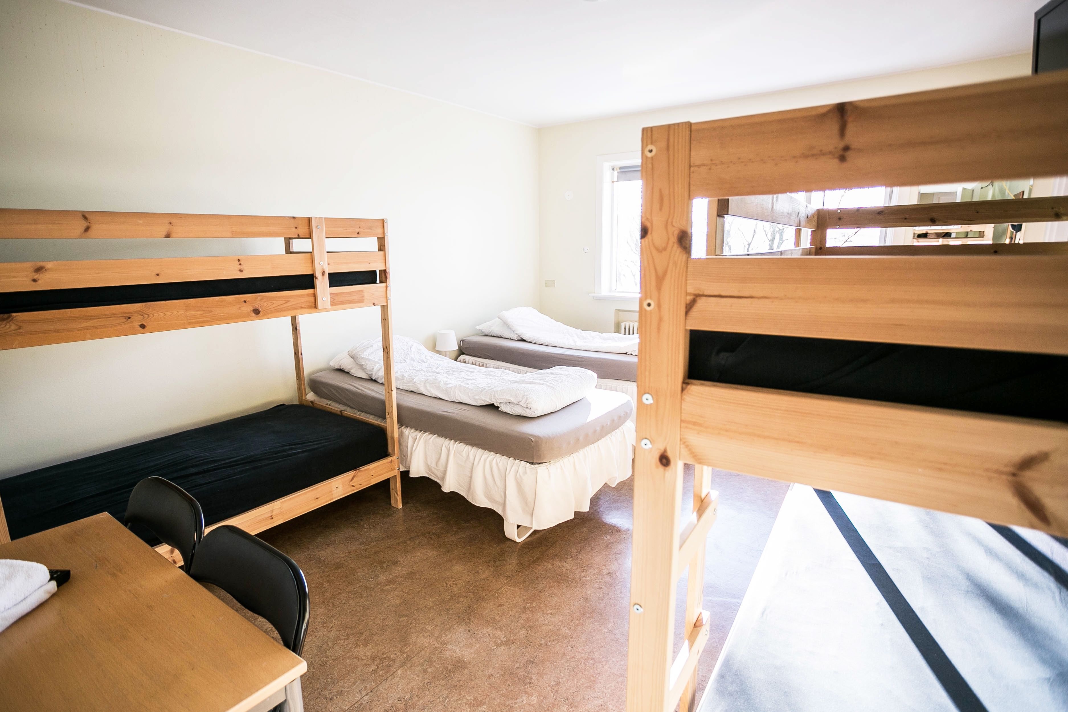 A dormitory room with bunk beds, a wooden desk, and a chair.